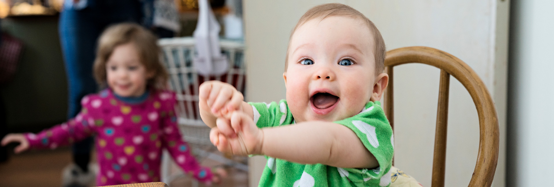 Happy baby sitting in chair, sibling in background